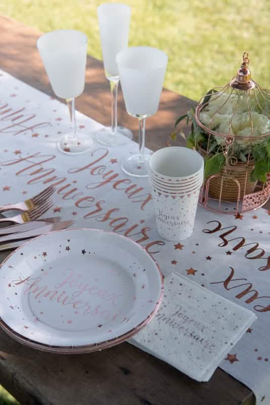 Mise en scène sur table de fête des assiettes en carton Joyeux Anniversaire blanches et rose gold à étoiles