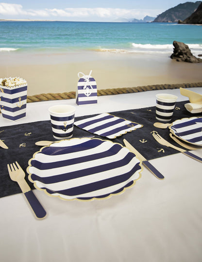 Mise en situation sur la plage des serviettes festonnées en papier marinière bleu marine et blanc à bords dorés avec ancre