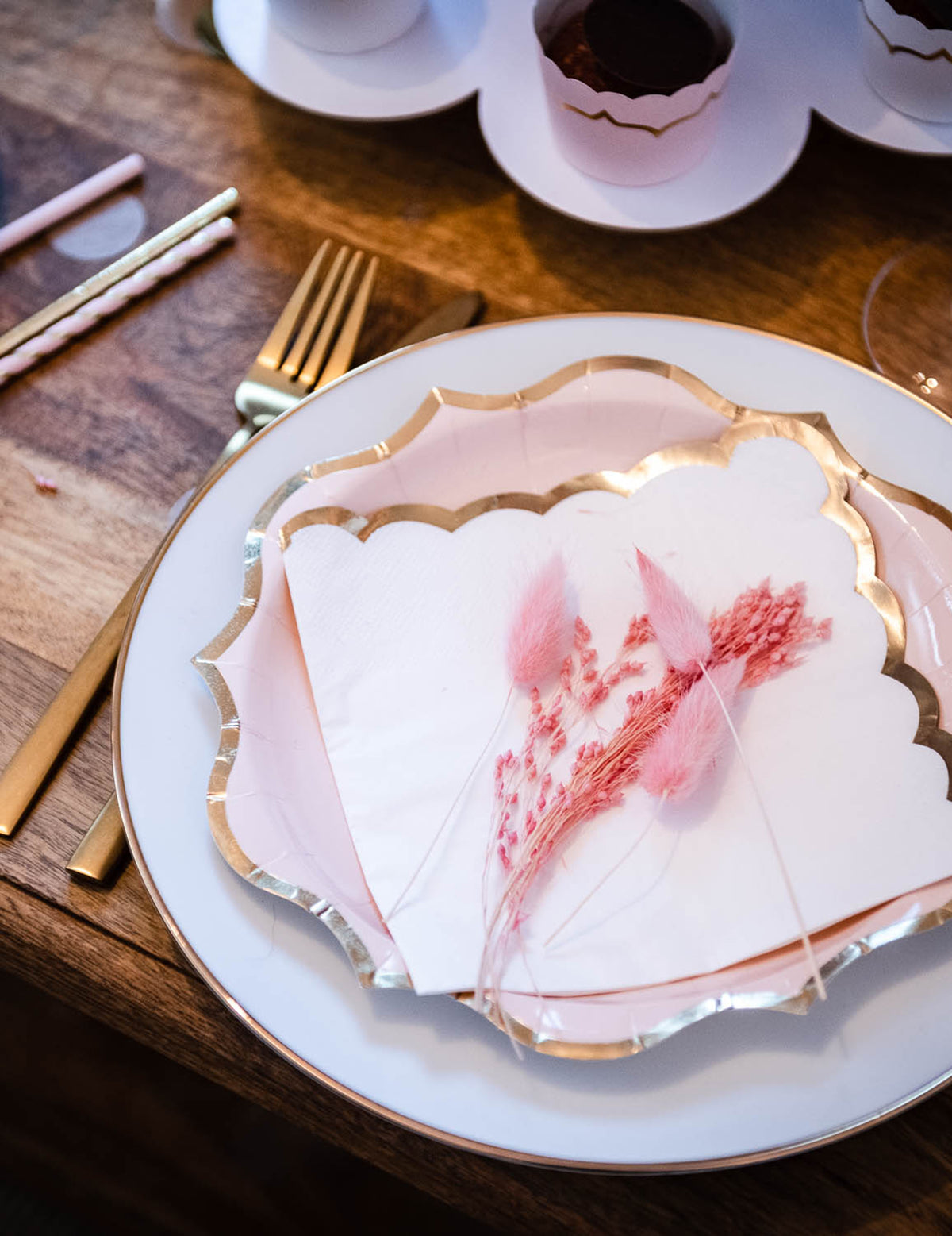 Mise en situation sur table des assiettes en carton rose poudré pour fête avec bordures dorées