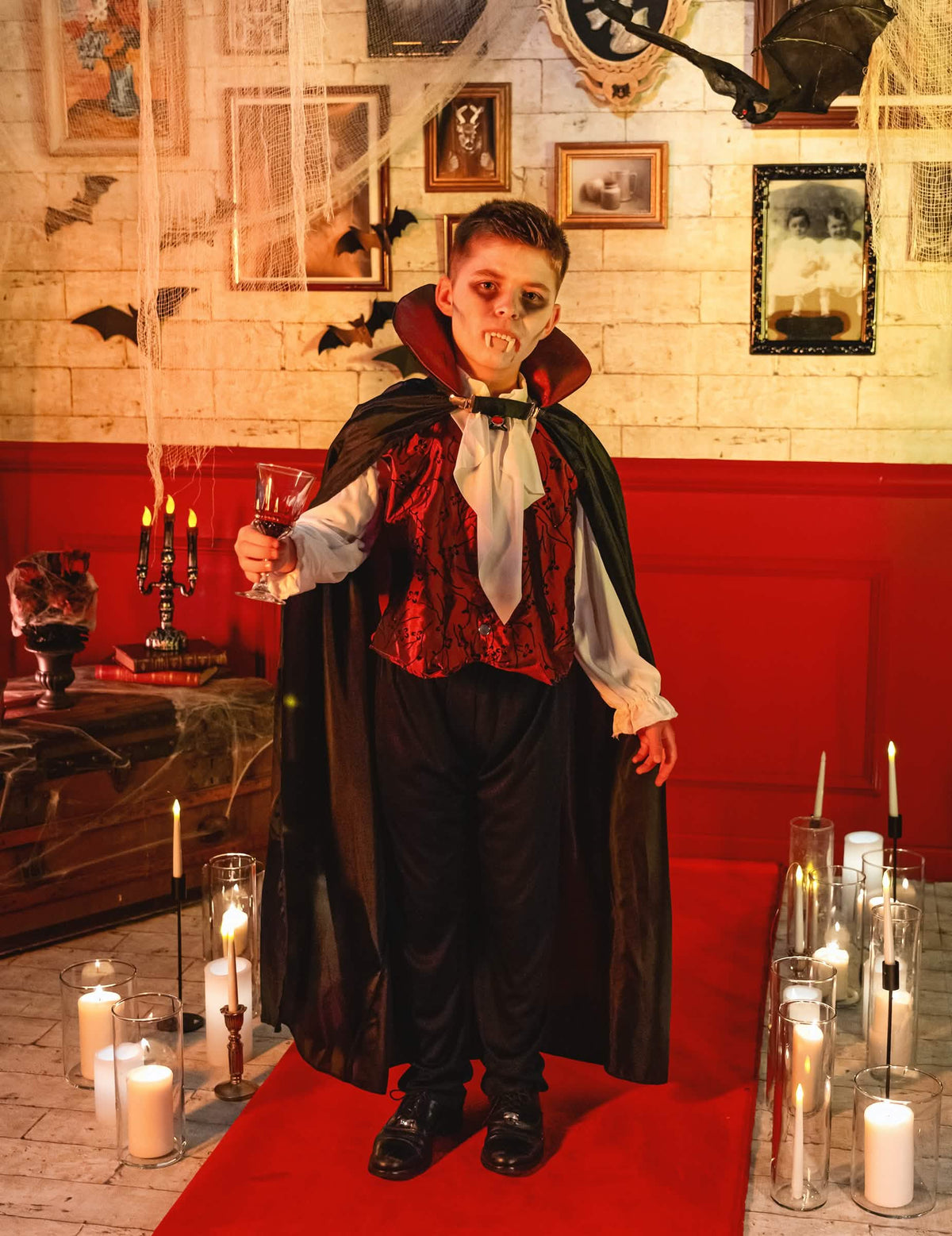 Elegáns vámpírfiú jelmez bemutatása halloweeni környezetben gyertyák között