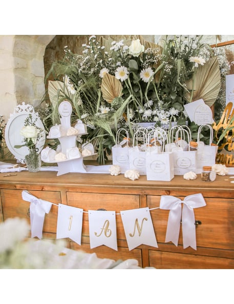 Mise en scène sur un buffet de la guirlande 1 an pour anniversaire blanche et dorée avec nœuds satinés