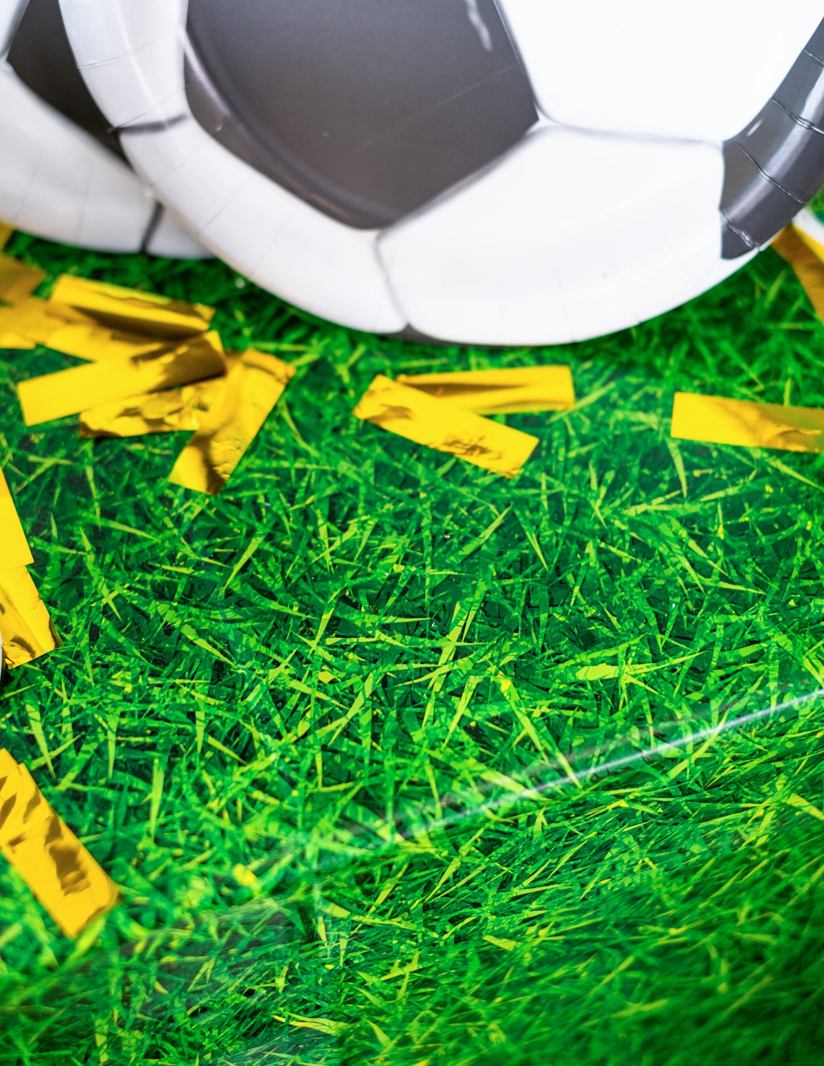 Détail des confettis dorés et de l'assiette ballon de la nappe effet herbe verte en plastique